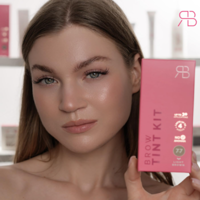 Mulher com pele clara segurando embalagem rosa de kit para sobrancelhas