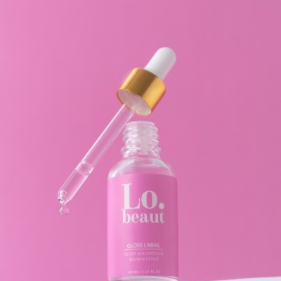 Frasco de gloss labial com conta-gotas sobre fundo rosa