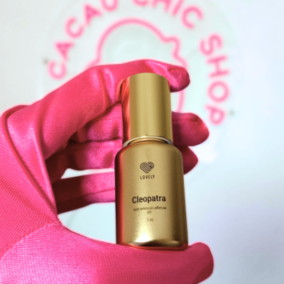 Frasco dourado de cola para pestanas com texto em mão com luva rosa