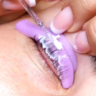 Olho com almofada ocular roxa e aplicação de produto branco nas pestanas superiores