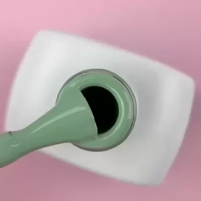 Pincel esponja verde e frasco branco para verniz em fundo rosa.