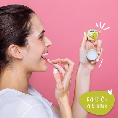 Mulher segurando pequeno pote amarelo de cosmético aberto com tampa e texto 15 ml em fundo rosa