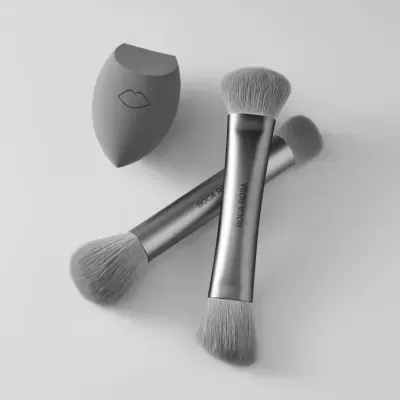 Dois pincéis de maquilhagem prateados e uma esponja cinzenta com desenho de lábios