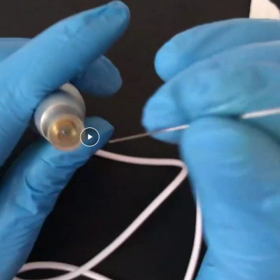 Mãos com luvas azuis segurando dispositivo cilíndrico com ponta dourada e cabo branco