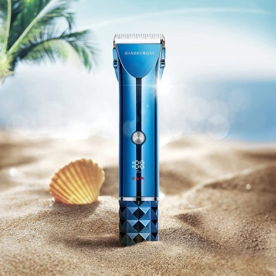 Máquina de cortar cabelo azul metálica na areia da praia com concha ao lado