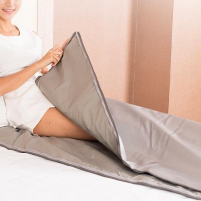 Pessoa sentada na cama usando edredão ou saco térmico cinzento com fechos laterais