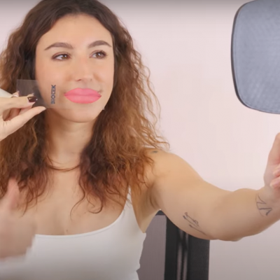 Mulher segura espelho e chocolate com palavra BLOCK, boca rosa desenhada.