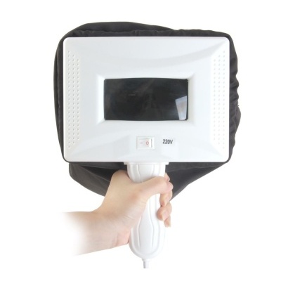 Aparelho branco com visor escuro e botão, 220V, segurado por uma mão grande com suporte preto