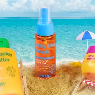 Frasco de spray laranja com tampa azul na areia da praia junto a outros produtos e mar ao fundo