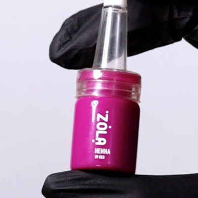 Frasco pequeno de Henna Zola vermelho com tampa transparente, sendo segurado por mão com luva preta