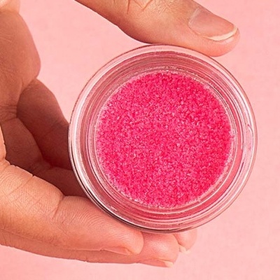 Frasco pequeno com pó granulado rosa segurado por mão em fundo cor-de-rosa