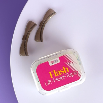 Caixa de fita adesiva Flash Lift-Hold-Tape e dois grampos de cabelo castanhos sobre fundo roxo e branco