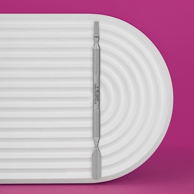 Espátula dupla em metal sobre base branca com fundo rosa