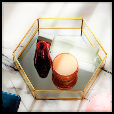 Bandeja hexagonal dourada com fundo espelhado e produtos de cosmética sobre uma superfície com padrão cinza