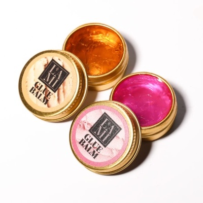 Duas latas pequenas com brilho corporal dourado e rosa, marcadas com 'GLITTER BALM'.