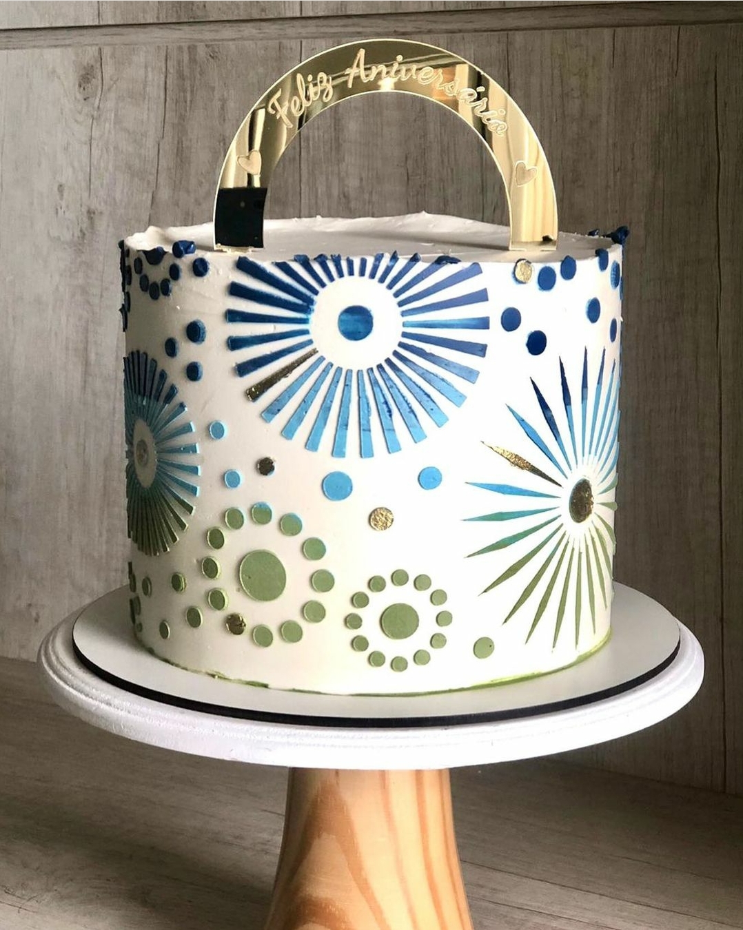 Bolo decorado com padrão azul e verde e toppers dourados com texto