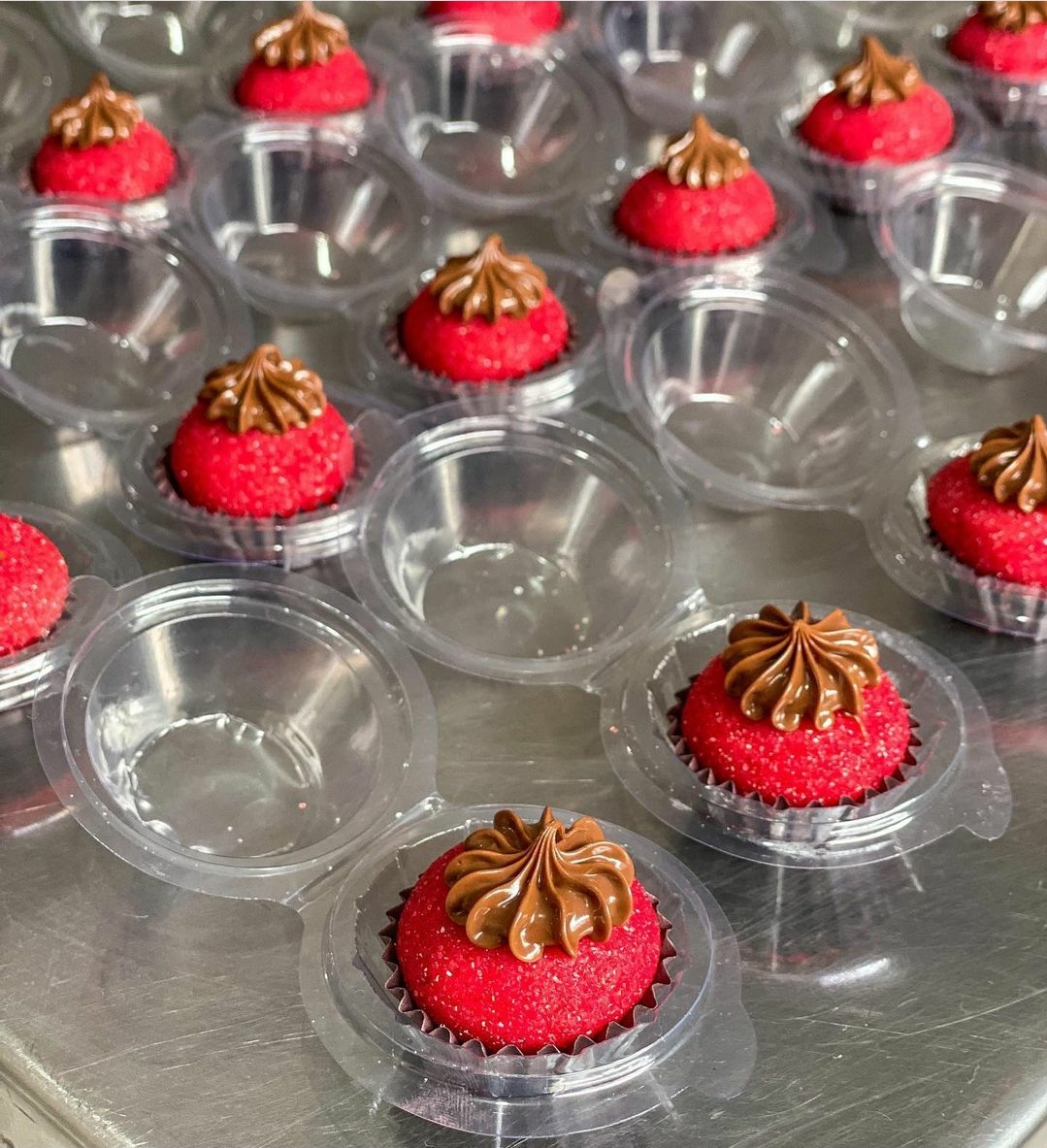 Pequenos bolos vermelhos com cobertura castanha em embalagens plásticas abertas sobre superfície metálica