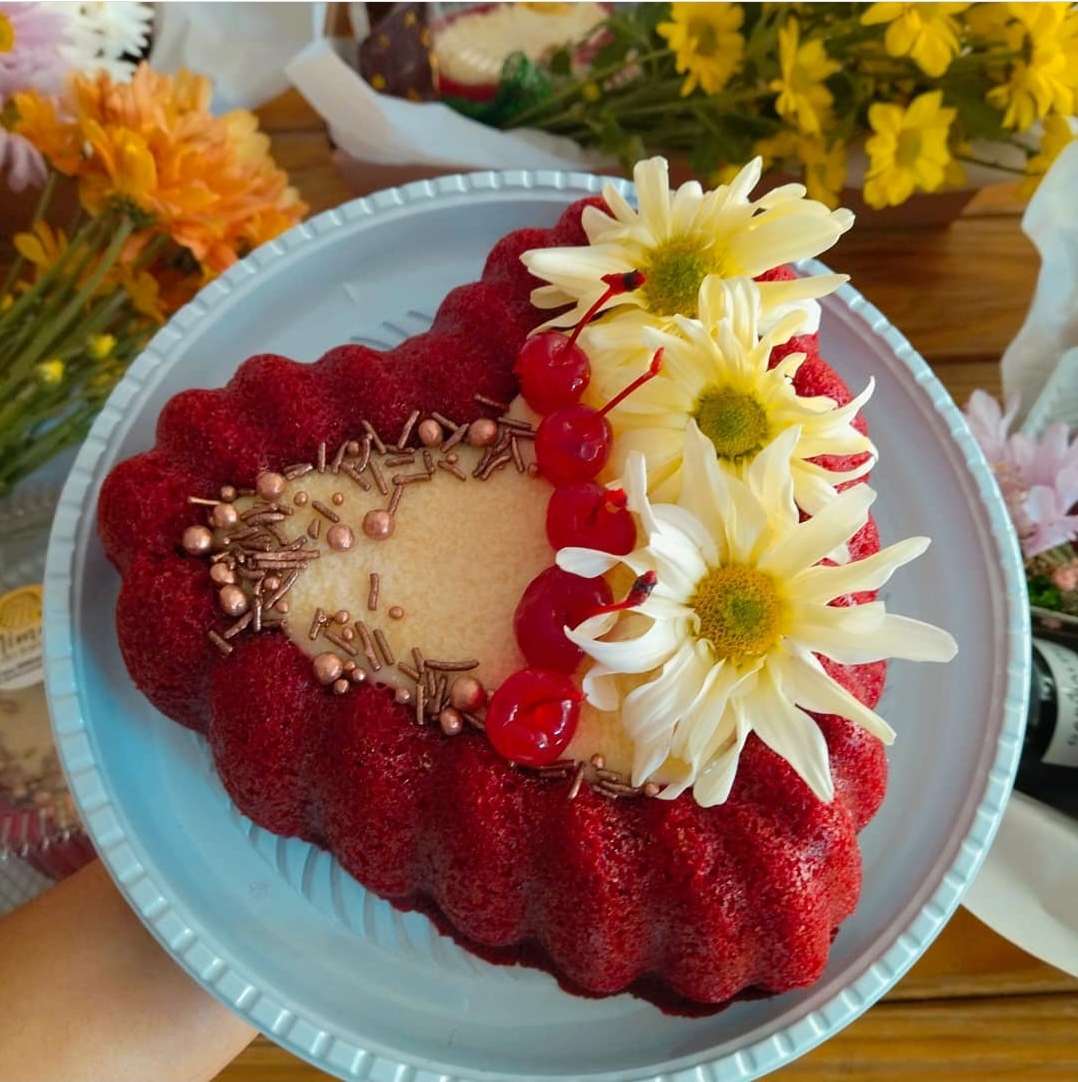 Bolo vermelho em forma de coração com decoração floral e cerejas