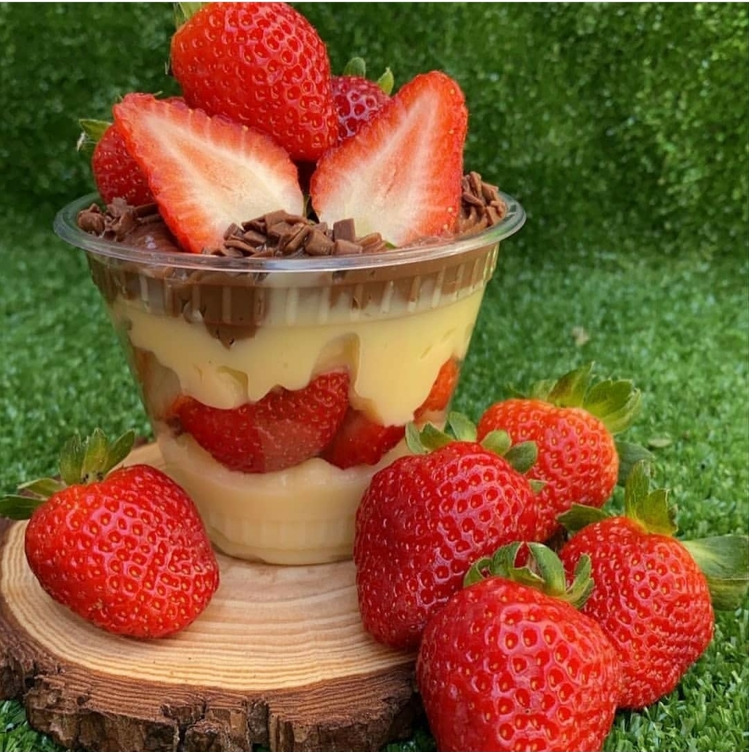 Sobremesa com morangos em copo transparente sobre base de madeira e morangos frescos