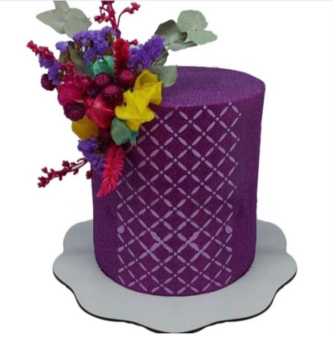 Bolo decorado roxo com padrão geométrico e flores artificiais coloridas no topo