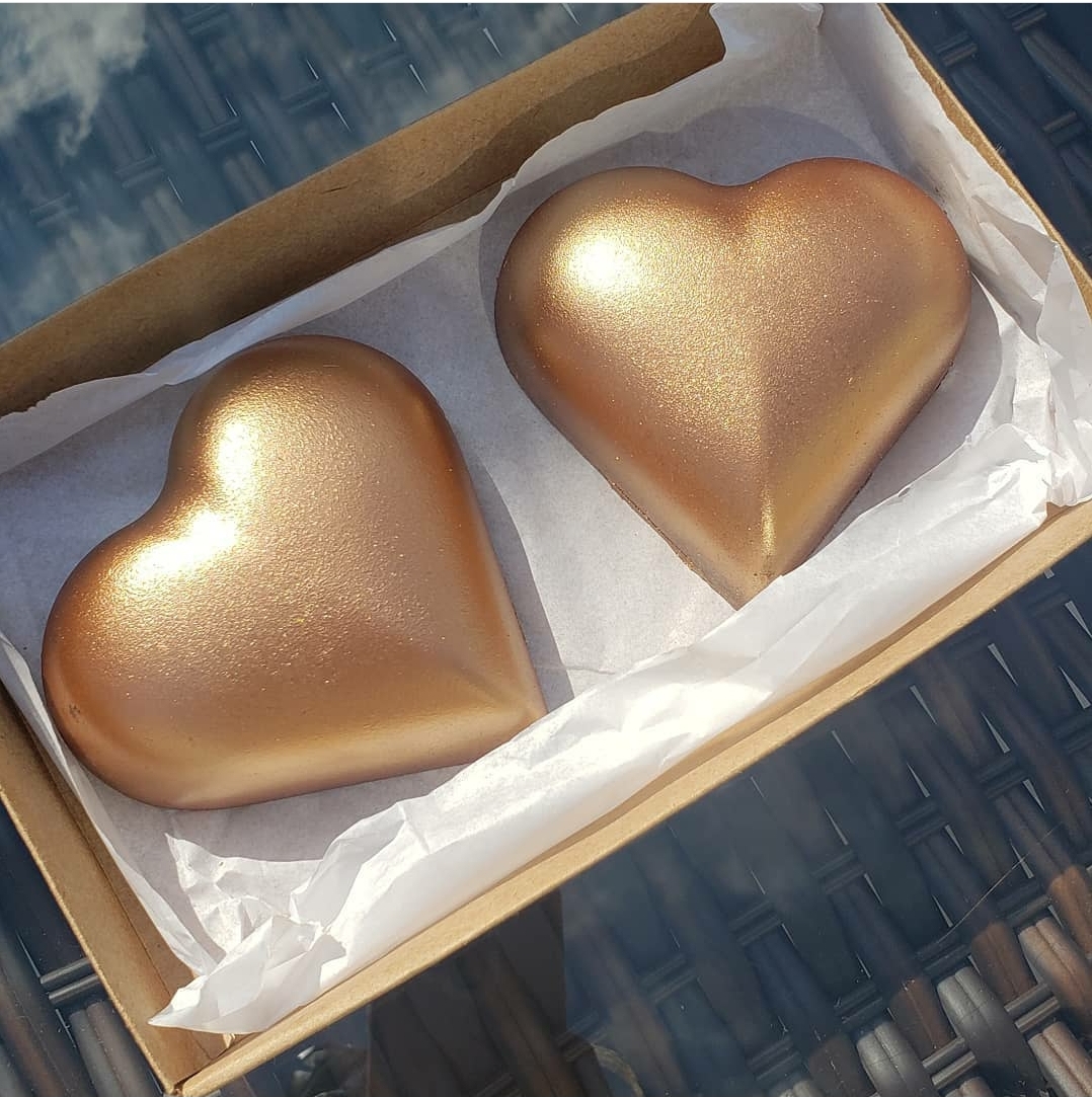 Dois corações dourados brilhantes numa caixa de cartão sobre superfície entrançada preta