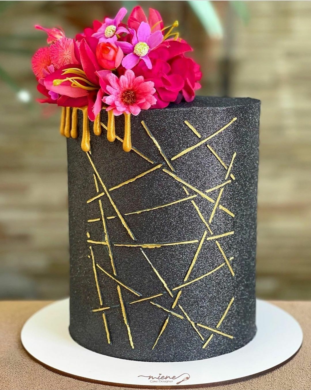 Bolo preto texturizado com decoração dourada e flores rosas no topo
