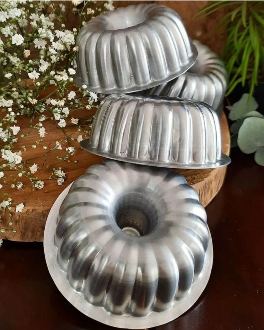 Formas de metal prateado para bolo com design canelado em mesa de madeira com flores brancas