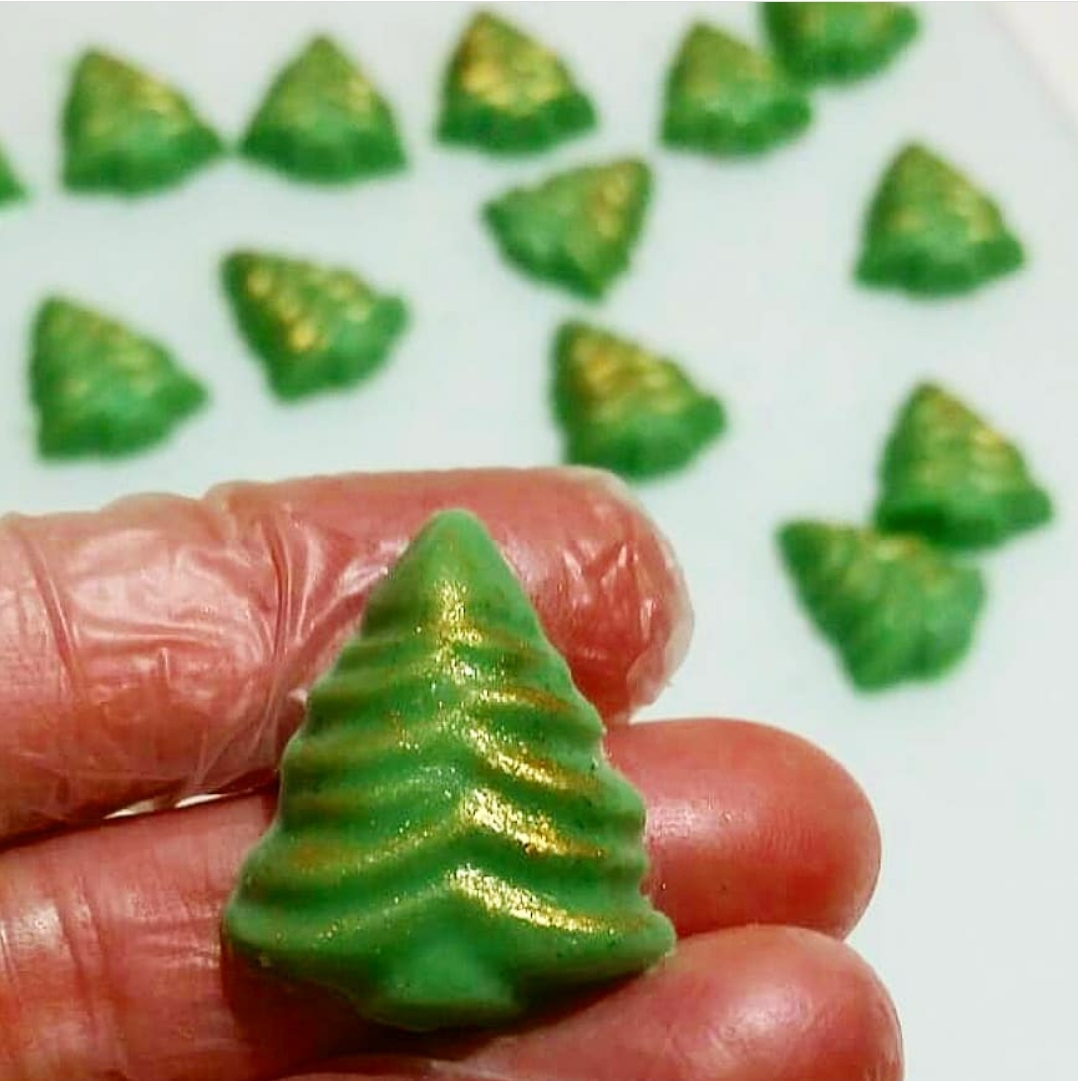 Chocolates verdes em forma de árvore de Natal com detalhes dourados segurados por mão enluvada