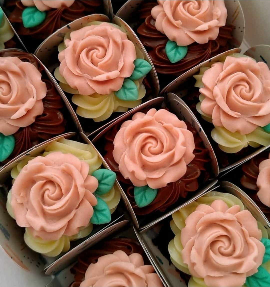 Cupcakes decorados com rosa cor-de-rosa e folhas verdes em caixas brancas