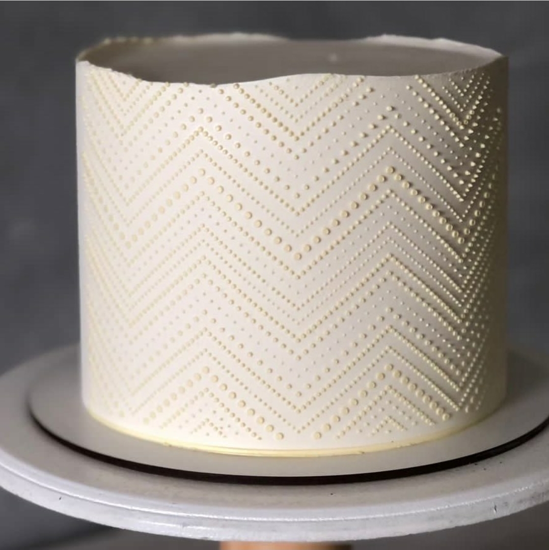 Bolo branco redondo com padrão de pontos dourados em ziguezague