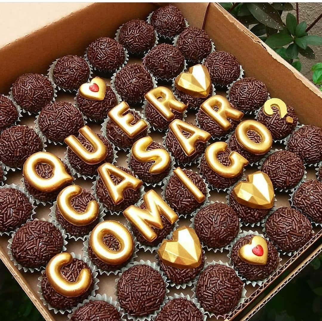 Brigadeiros e chocolates em forma de letras douradas com frase romântica numa caixa de cartão