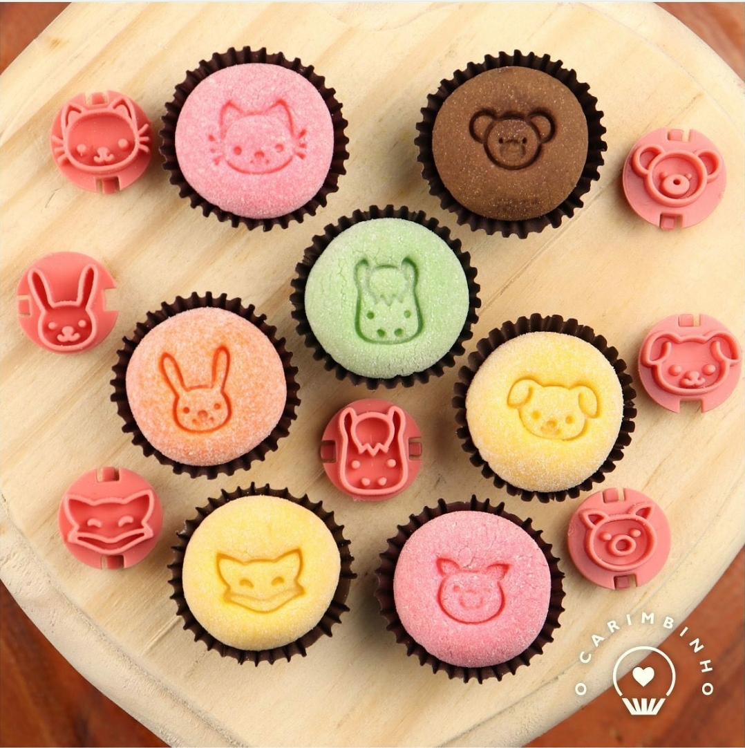 Cupcakes coloridos com estampas de animais em relevo e moldes de silicone cor-de-rosa com formas de rosto de animais sobre tábua de madeira.