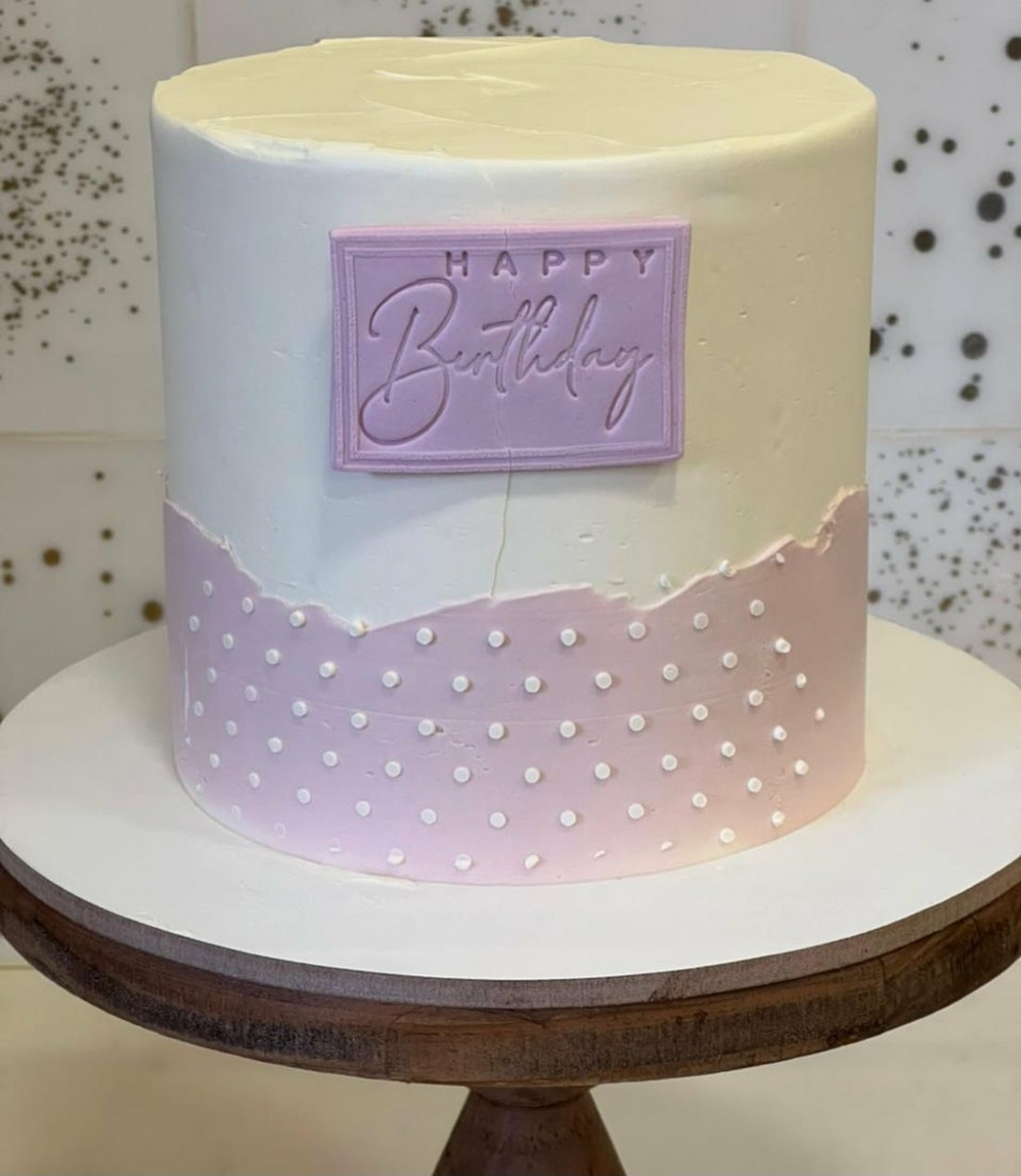 Bolo redondo branco e rosa com pontos brancos e placa HAPPY Birthday