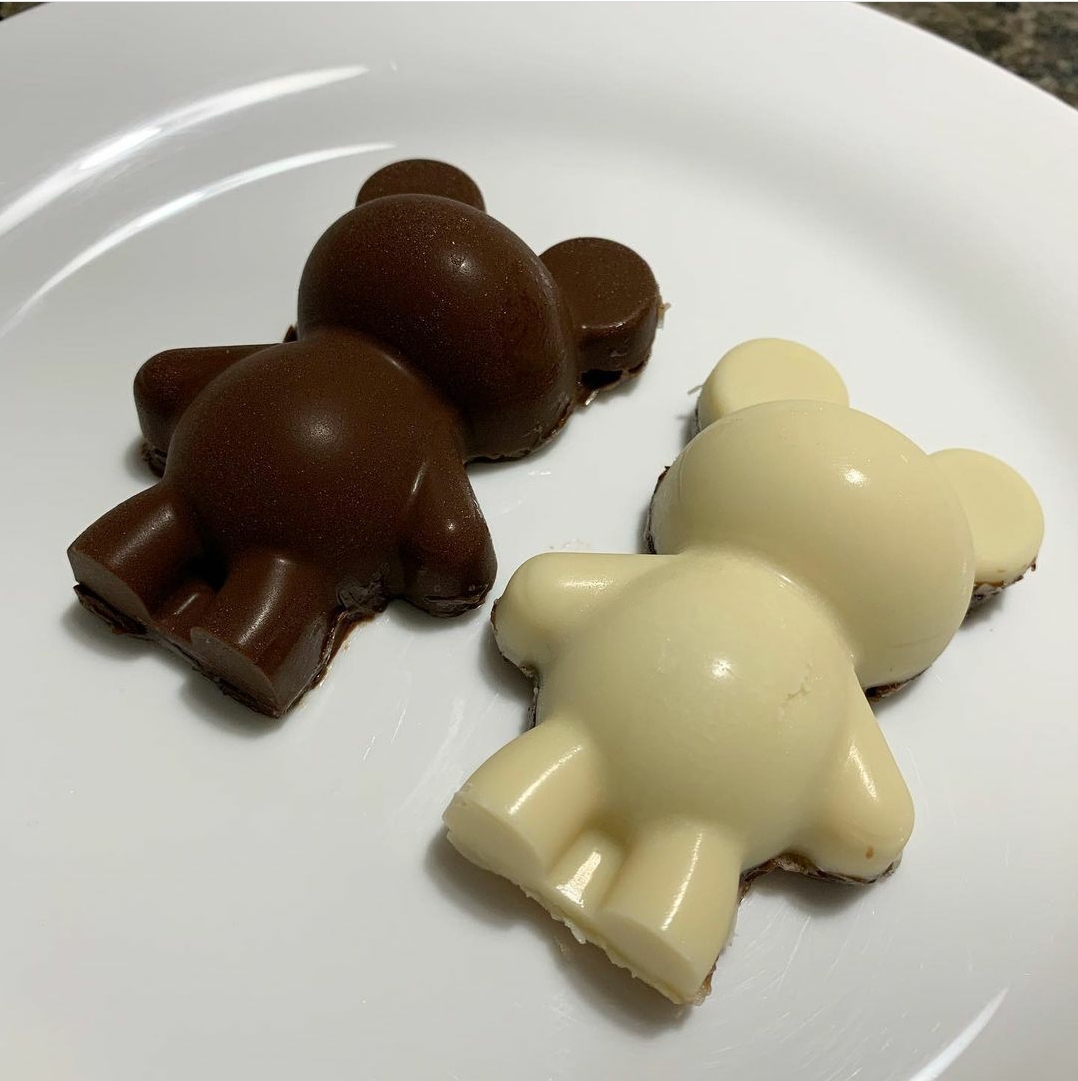 Dois chocolates em forma de ursinho, um branco e outro ao leite, sobre prato branco.