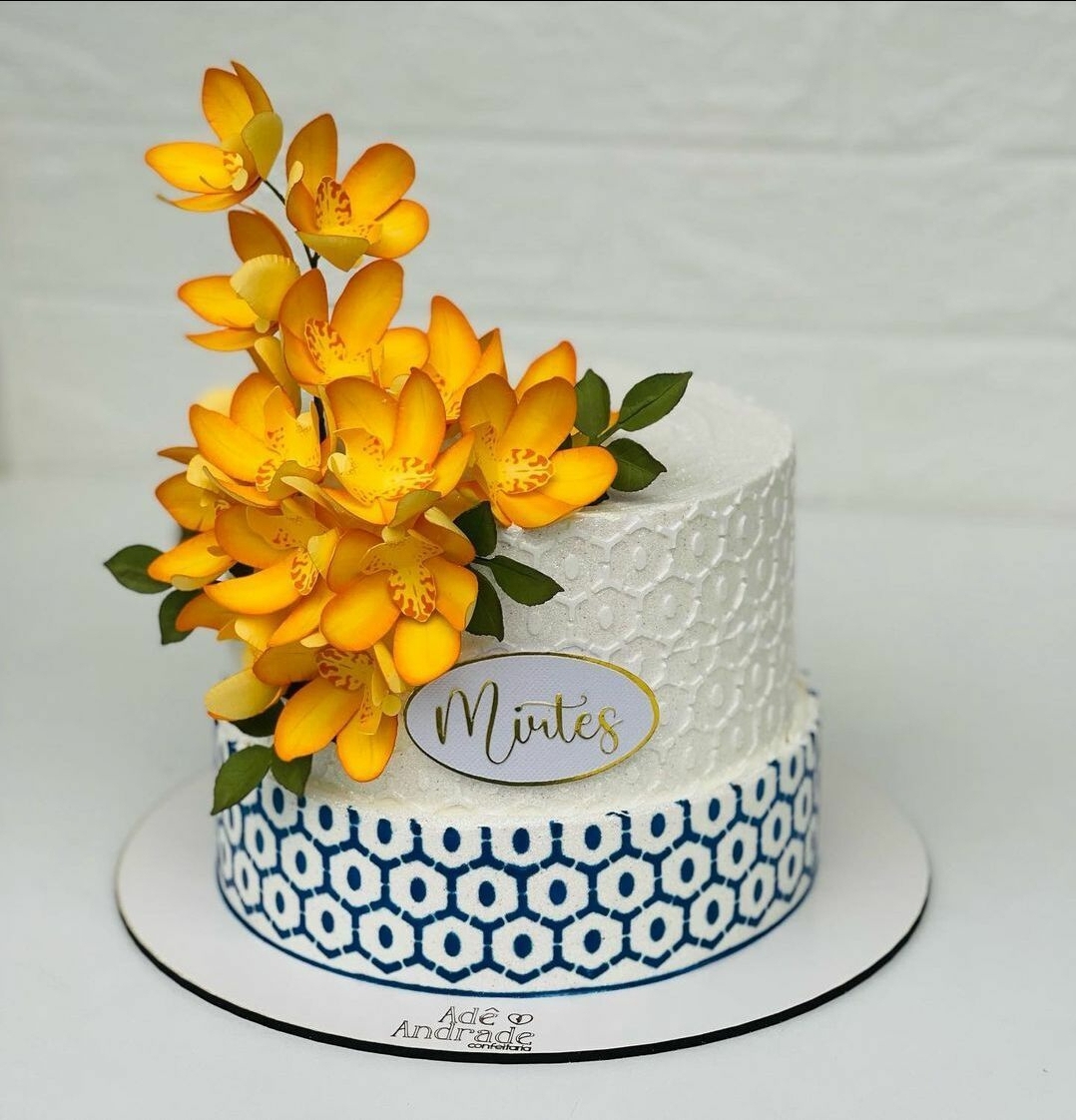 bolo decorativo branco e azul com flores amarelas e placa com nome