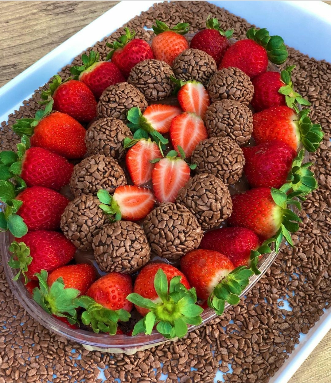 Tigela transparente com brigadeiros e morangos frescos sobre bandeja branca