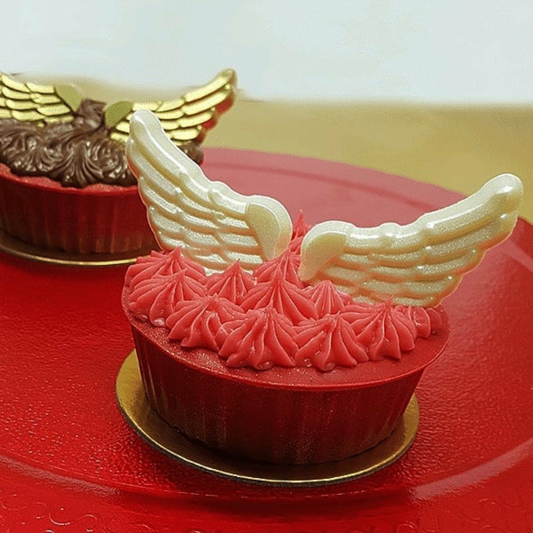 Dois cupcakes vermelhos com asas de chocolate branco e dourado numa base vermelha.