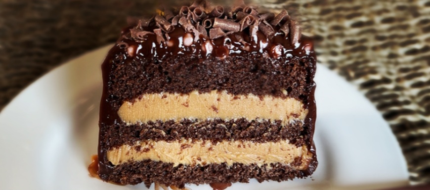 Pedaço de bolo de chocolate com recheio amarelo claro e cobertura de chocolate