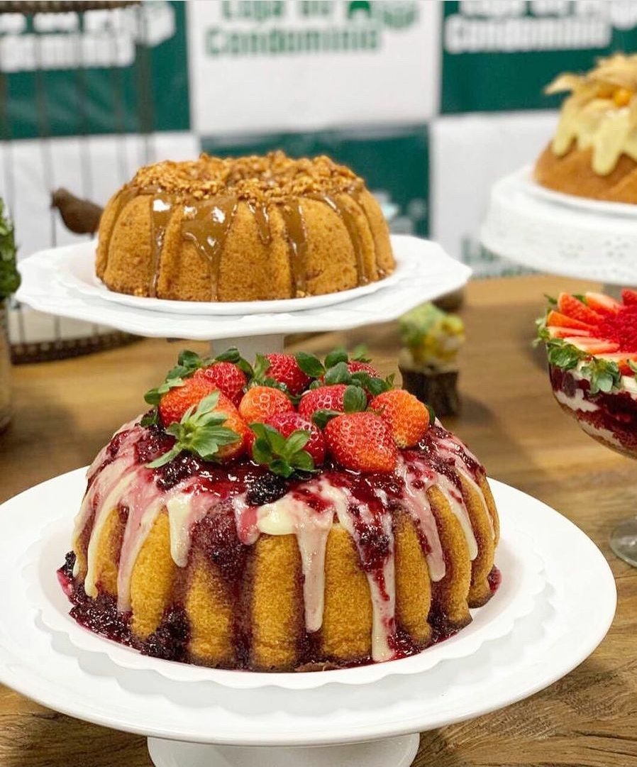 Dois bolos bundt decorados, um com morangos e glacê branco e vermelho e outro com cobertura castanha granulada em pratos brancos