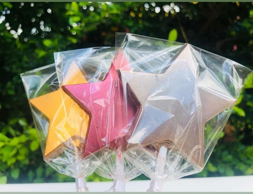 Pirulitos em forma de estrela com cores amarelo, rosa e prateado embalados em plástico