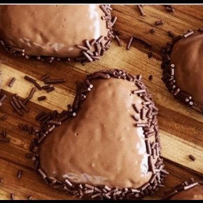 Biscoitos em forma de coração com cobertura de chocolate e granulados de chocolate sobre tábua de madeira