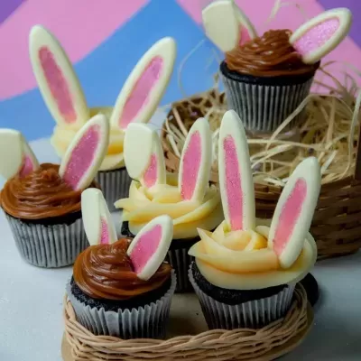 Cupcakes decorados com orelhas de coelho em creme e chocolate, em cestos de vime.