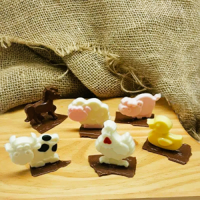 Figuras de animais em chocolate branco e chocolate de leite sobre tabuleiro de madeira com fundo de serapilheira