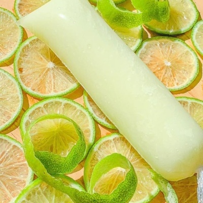 Picolé branco em cima de rodelas de lima verde com casca enrolada num fundo de madeira