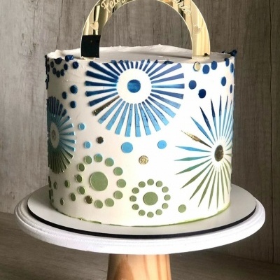 Bolo decorado com padrão azul e verde e toppers dourados com texto