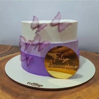 Bolo redondo com decoração de borboletas e placa dourada com texto
