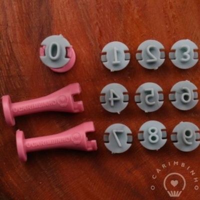 Carimbos plásticos rosa e cinza com números de 0 a 9 sobre madeira
