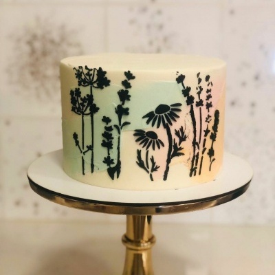 Bolo branco com silhuetas pretas de flores em suporte dourado redondo