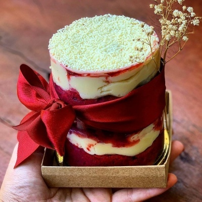 Bolo redondo em camadas com fita vermelha e decoração seca em caixa de cartão