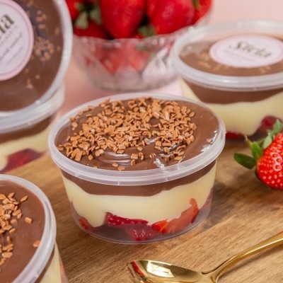 Sobremesa em copo transparente com camadas de chocolate, creme e morangos, com coberturas de chocolate granulado e colher dourada